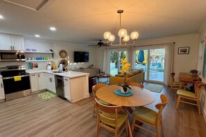 A modern kitchen with a central island, a dining area with a round table, and a living space with a sofa and a TV. - Waterfront Bungalow Getaway | Sleeps 12 (Madeira Beach)