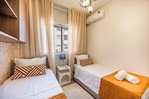 Une chambre d’hôtel avec deux lits simples, une petite table avec une lampe et un appareil de climatisation fixé au mur.