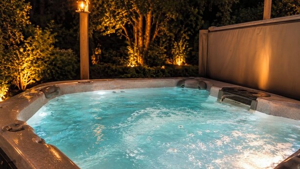 A hot tub with a wooden structure and a metal railing, surrounded by greenery. - Knot Northern Retreat & Spa: Hot Tub • Gym • Workspace (Minneapolis)