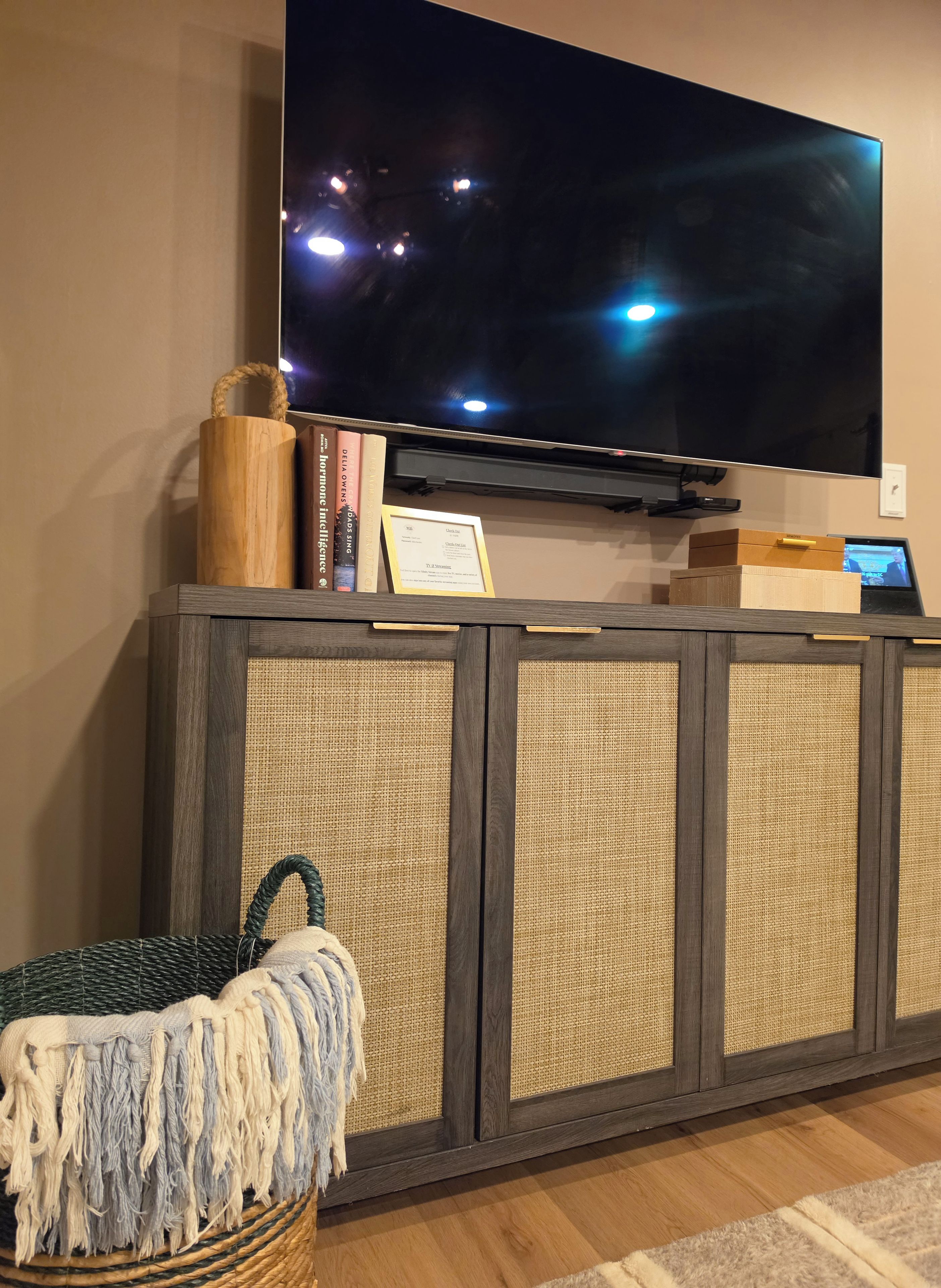 Un téléviseur à écran plat fixé au mur, au-dessus d’une console en bois, avec un panier en osier et des livres.