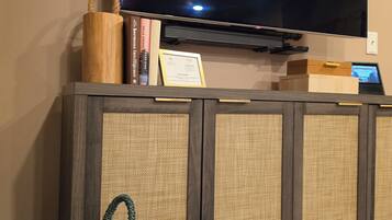 Een flatscreen televisie bevestigd aan een wand boven een houten dressoir met een gevlochten mand en boeken.