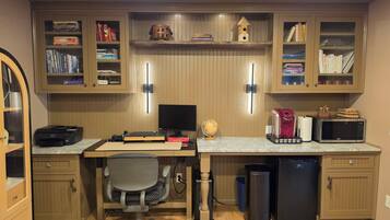 A home office with a desk, computer, bookshelf, and various office supplies.