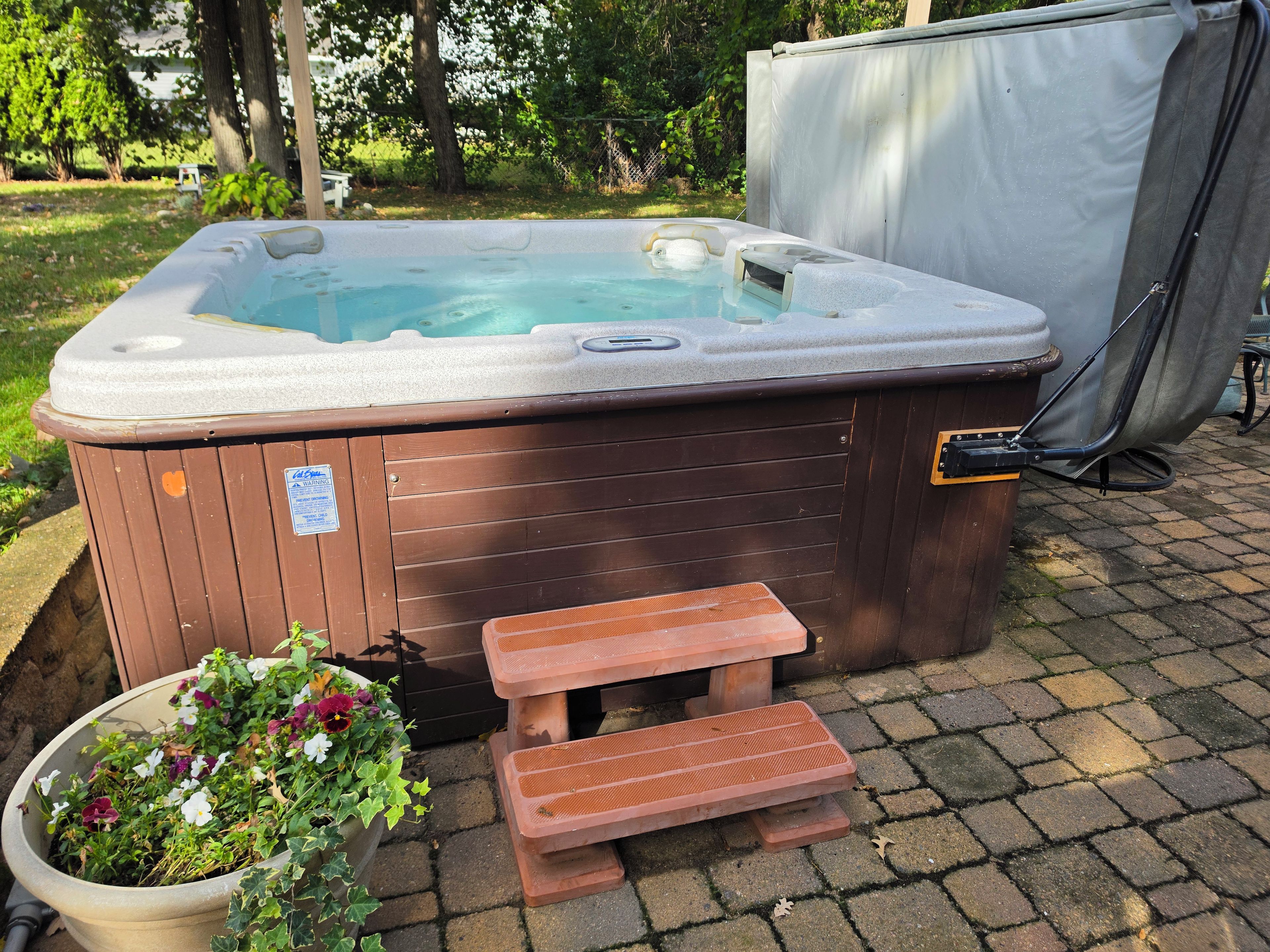 A hot tub with a wooden bench and a step, surrounded by a garden with flowers.