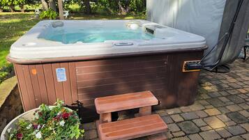 A hot tub with a wooden bench and a step, surrounded by a garden with flowers.