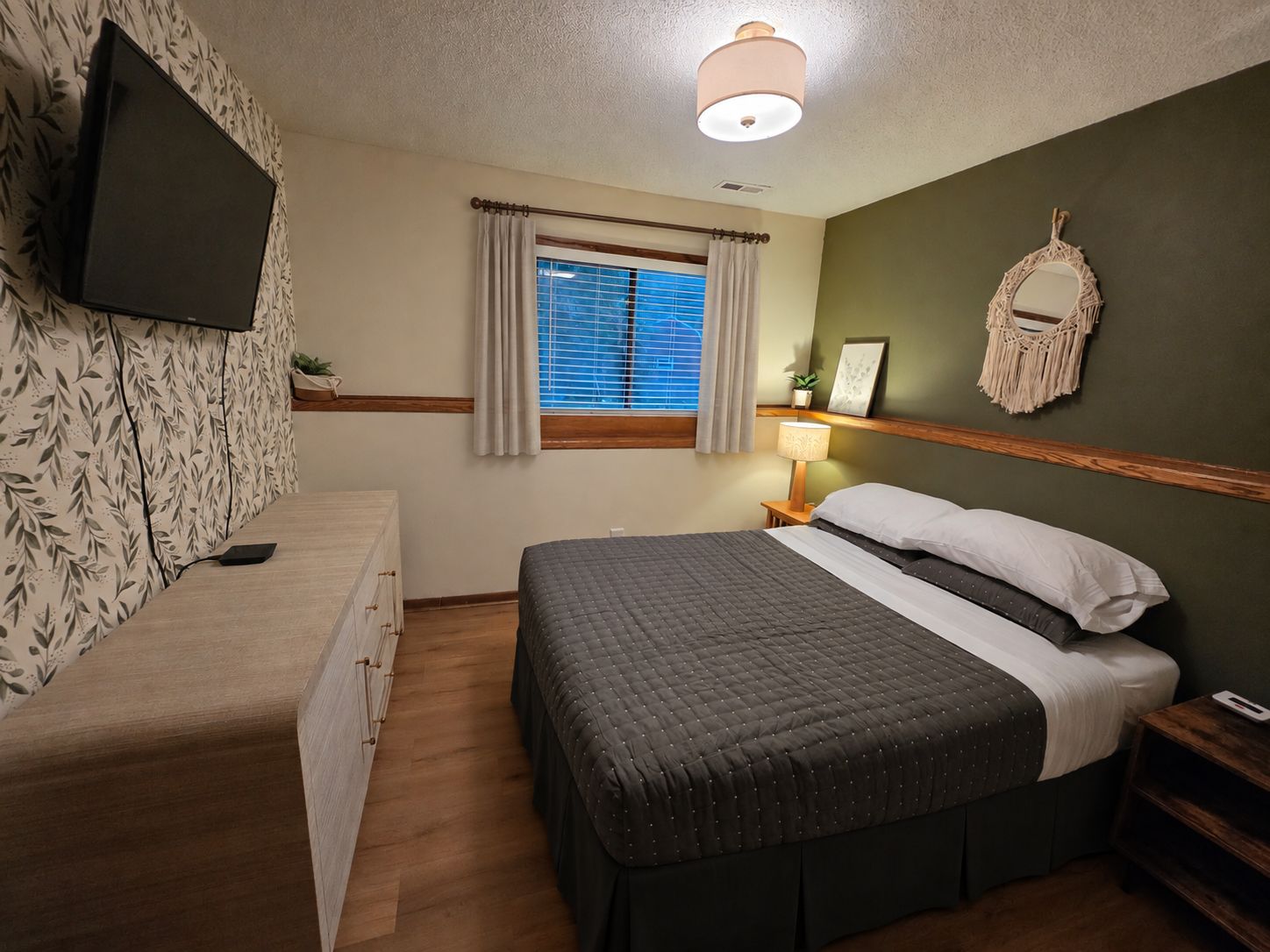A bedroom with a bed, bedside table, lamp, and a wall-mounted TV.