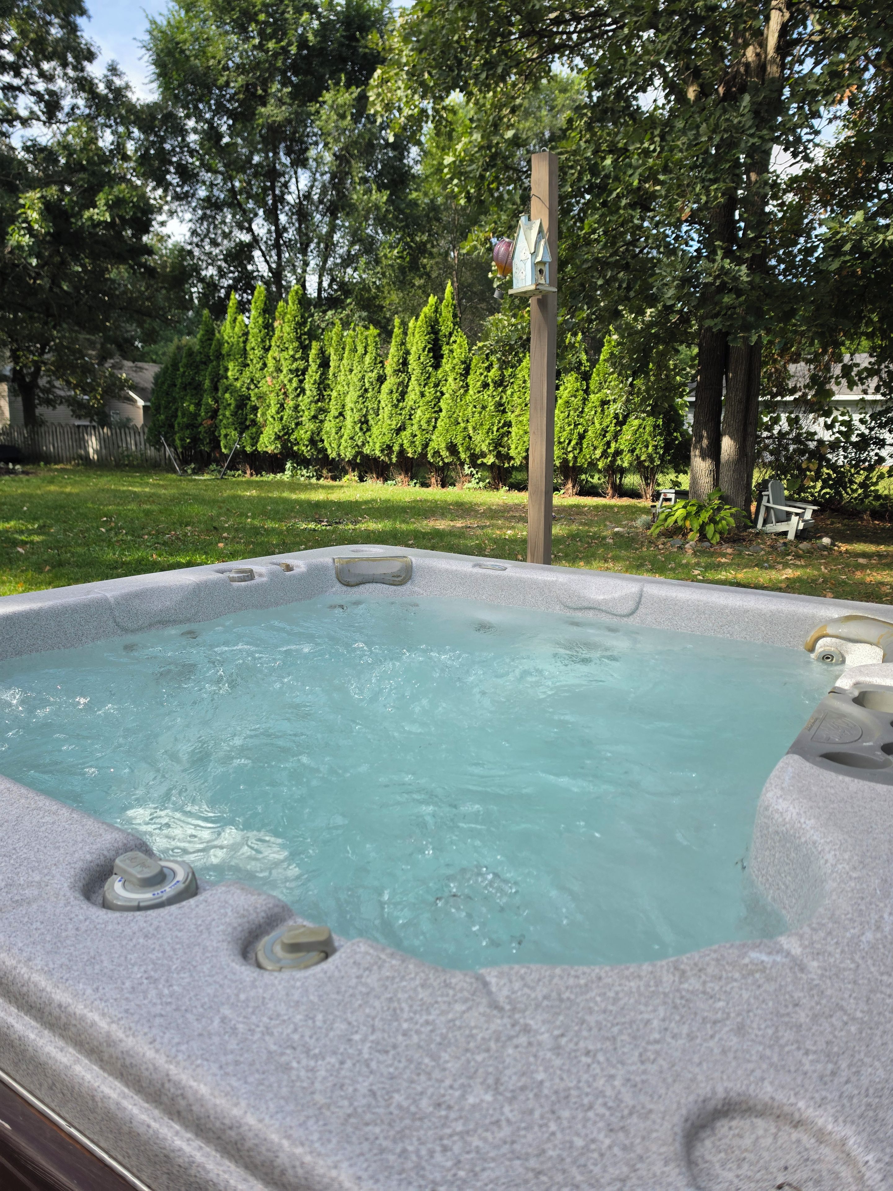 A hot tub with a wooden deck and a birdhouse in the background.