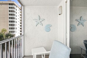 A balcony with a white chair, a small table, and decorative starfish wall art. - Gulf view studio, walk to beach, shared pool & full kitchen (Bonita Springs)