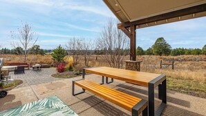Ein Außenbereich mit einer Holzterrasse, einem Tisch, Bänken, einem Grill und einer Steinmauer.