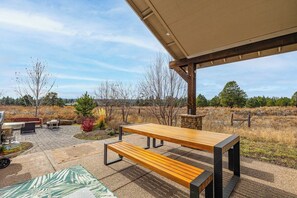An outdoor patio area with a wooden table and benches, a grill, and a stone wall. - Wolfmoor spacious cabin with trail access (Flagstaff)