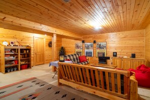 A cozy log cabin interior with a wooden ceiling, a sofa, a small table, and a bookshelf.