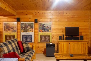 A cozy room with a wooden ceiling and walls, a sofa with patterned cushions, a television on a wooden cabinet, and framed calendars on the wall.