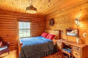 A log cabin bedroom with a bed, dresser, and a window.
