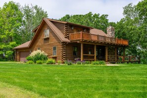 A log cabin with a balcony, surrounded by a well-maintained lawn and trees. - Skyline Log Cabin • River Views + Screened Patio (Wabasha)