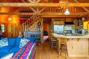 L’intérieur d’une cabine est aménagé avec un escalier en bois, un canapé agrémenté de coussins colorés, un coin cuisine comprenant un réfrigérateur et une cuisinière, ainsi qu’un bar avec des tabourets.