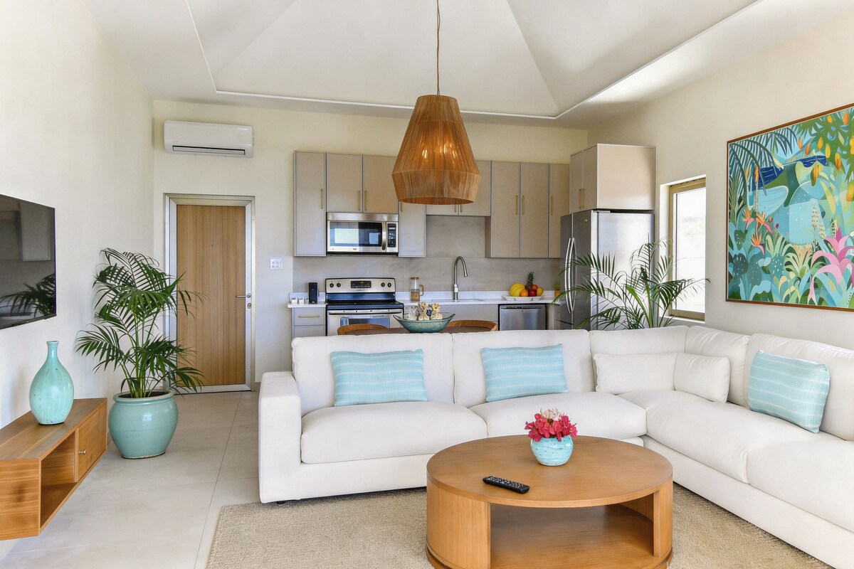 Una sala moderna con un sofá blanco, una mesa de centro de madera y una cocina al fondo.