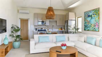 A modern living room with a white sofa, a wooden coffee table, and a kitchen in the background.