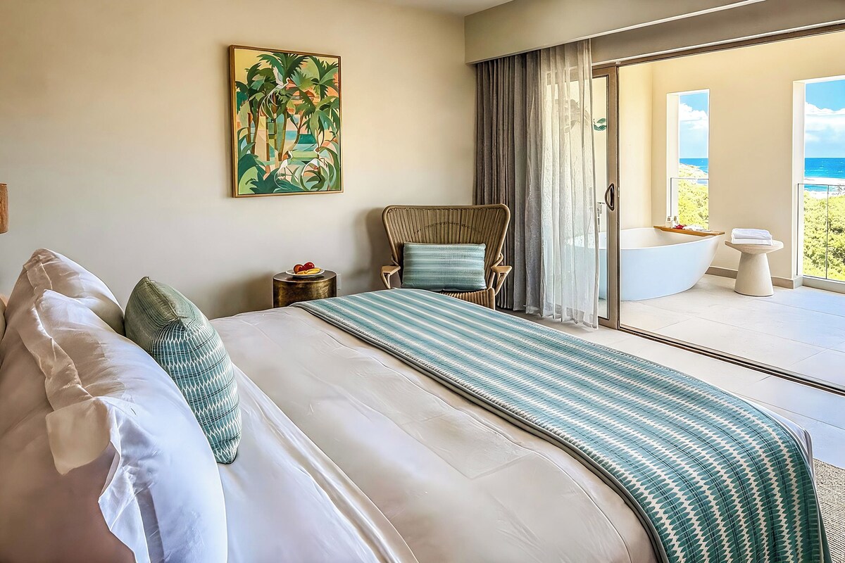 Habitación de hotel con una cama grande, vista al mar, un cuadro en la pared y un baño con bañera.