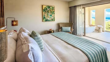 A hotel room with a large bed, a view of the sea, a painting on the wall, and a bathroom with a bathtub.