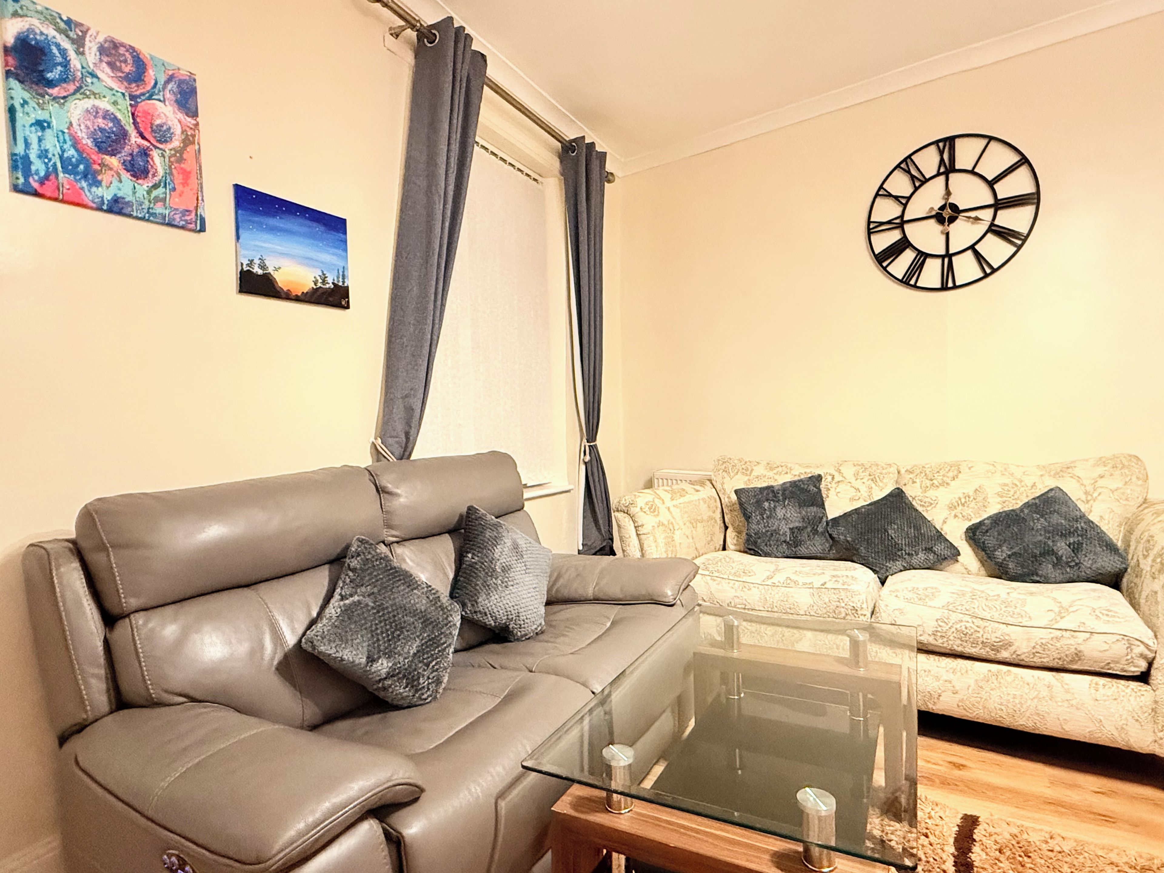 A living room with a leather sofa, a glass coffee table, and a patterned sofa.