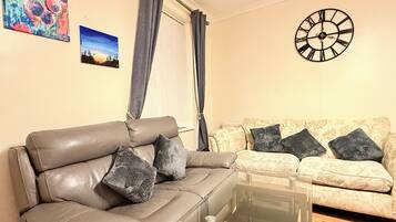 A living room with a leather sofa, a glass coffee table, and a patterned sofa.