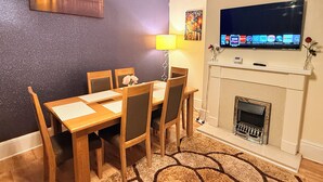 En matplats med ett bord och stolar, en öppen spis och en tv som är monterad på väggen.