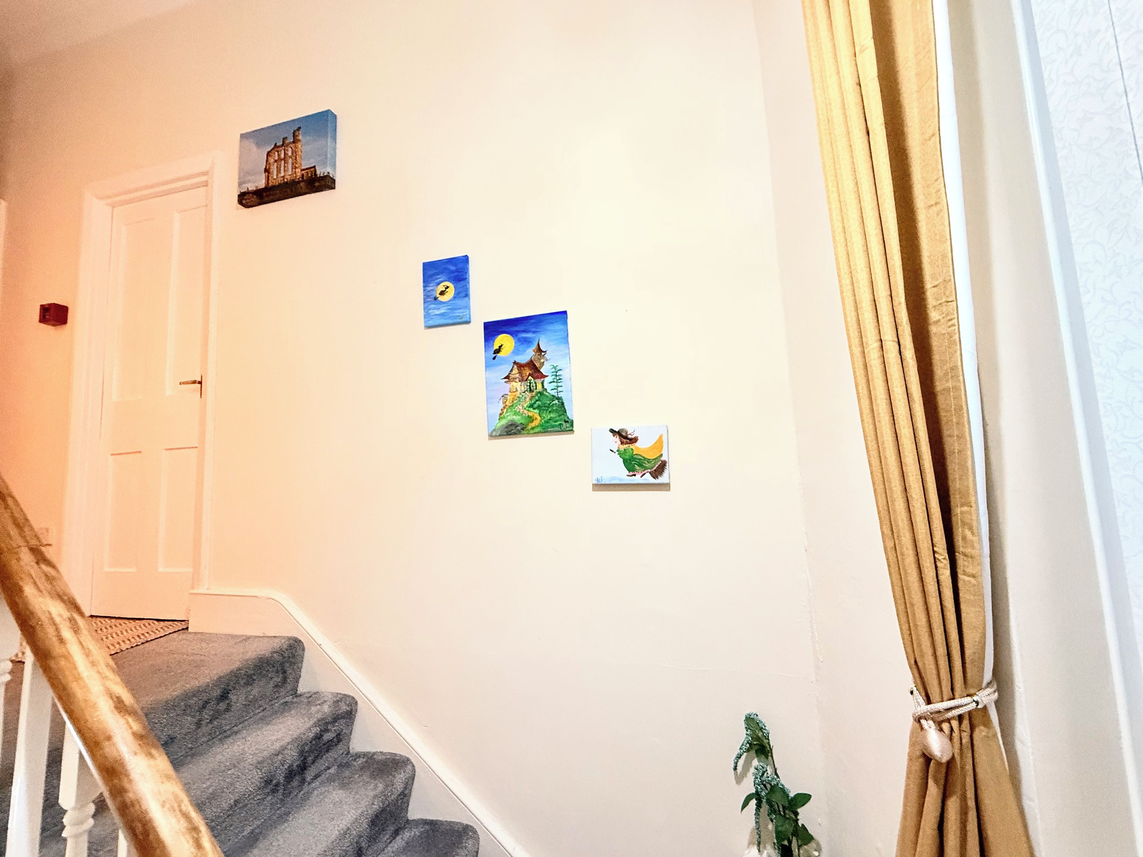 A staircase with a handrail, a door, and three framed pictures on the wall.