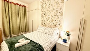 Ett hotellrum med en säng, ett nattduksbord, en spegel, ett fönster med gardiner och en blommig tapet.