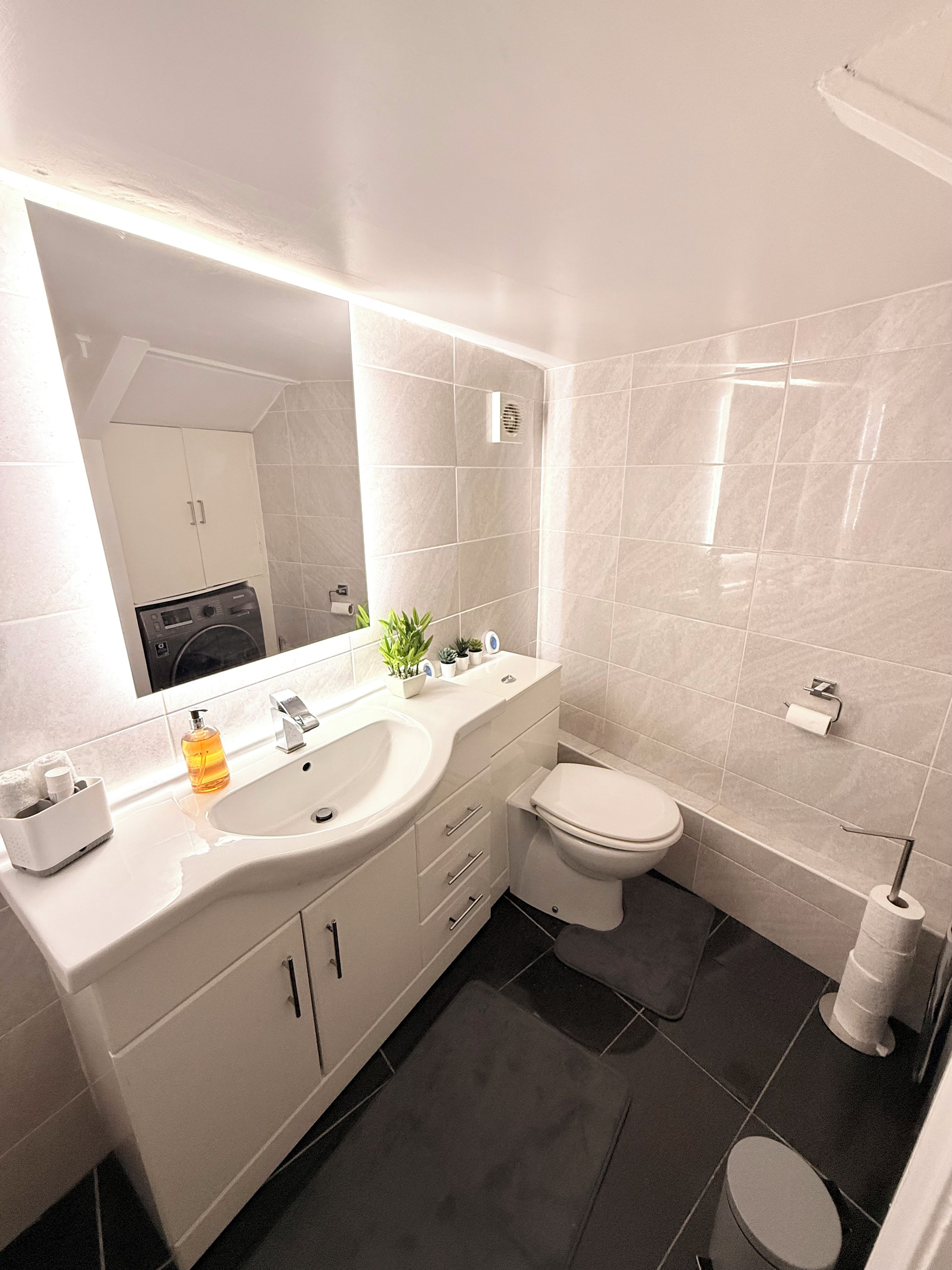 A modern bathroom with a white sink, mirror, and toilet.