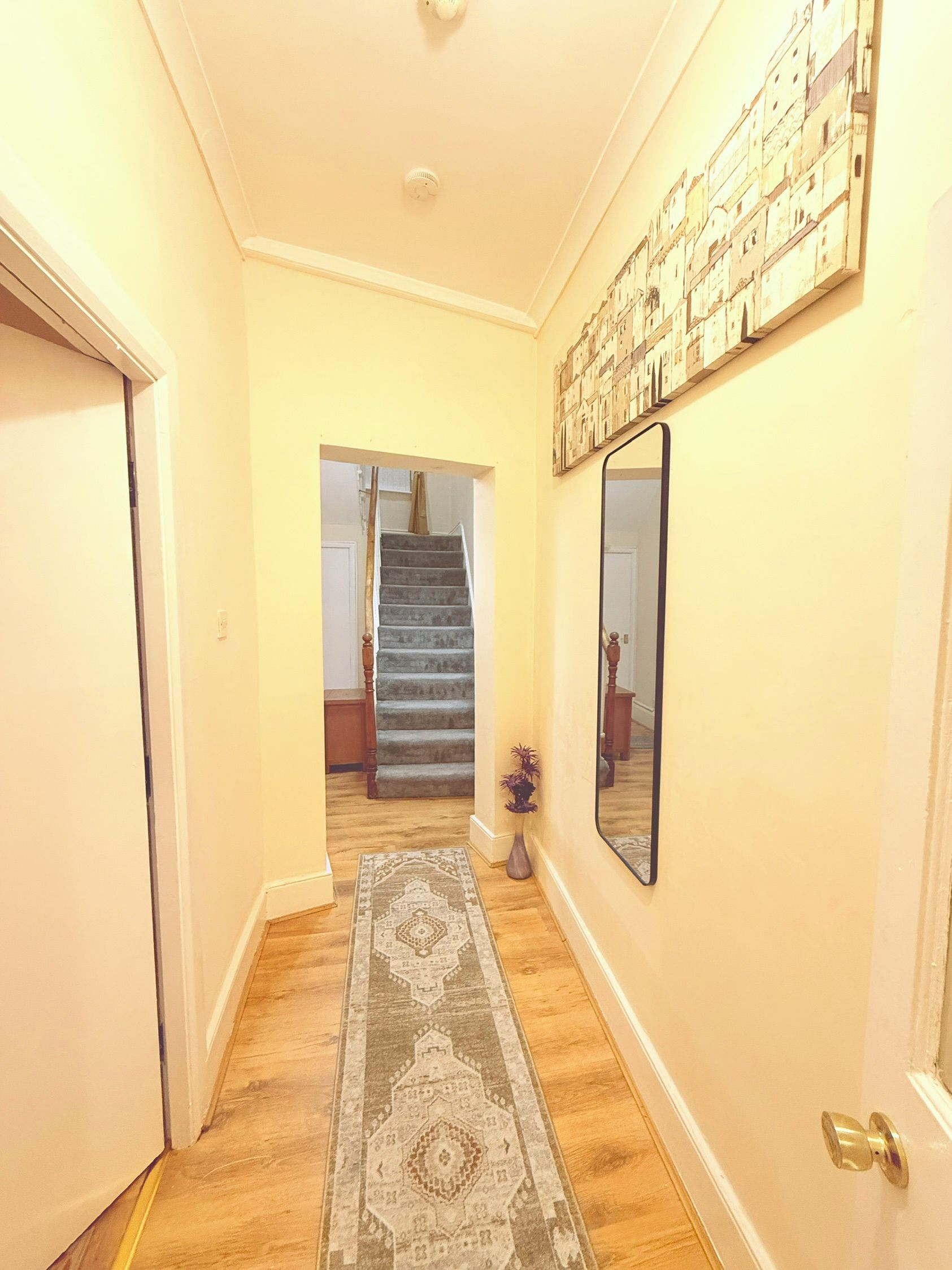 Un couloir avec un tapis, un escalier et un miroir fixé au mur.