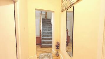 A hallway with a carpet, a staircase, and a wall-mounted mirror.
