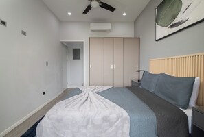A bedroom with a bed, a bedside table, a nightstand, a ceiling fan, an air conditioning unit, and a door leading to another room. - Hilltop Paradise with Pool: 3BR in Playa del Coco (Coco)
