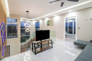 A modern living room with a flat-screen TV, a glass staircase, and a balcony with a view. - Hilltop Paradise with Pool: 3BR in Playa del Coco (Coco)