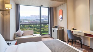 A hotel room with a large window, a bed, a desk, a chair, and a small cabinet. - Yannian Hangmai Hotel (Changsha)