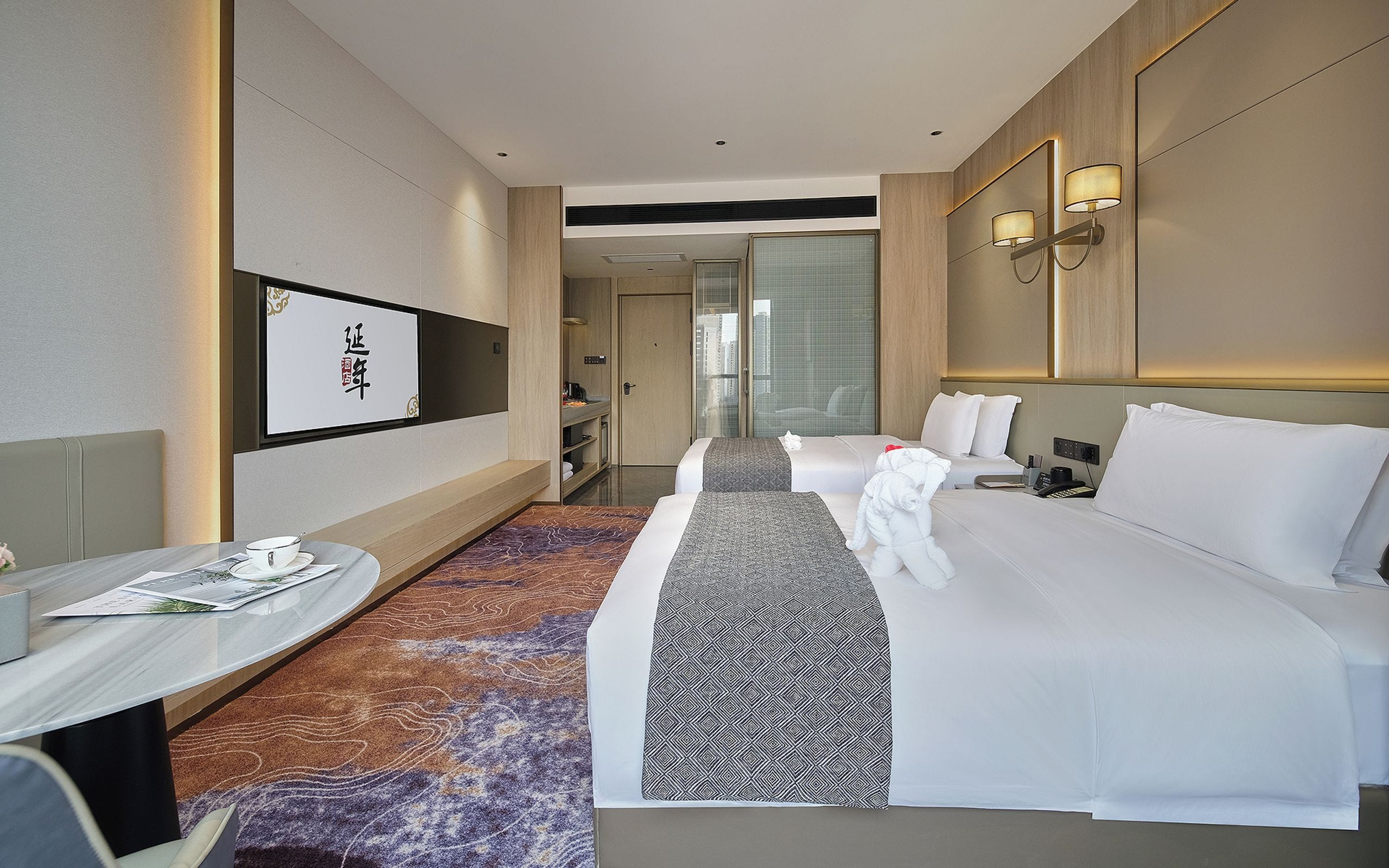 Quarto de hotel com cama, mesa de cabeceira, abajur e vista para a cidade pela janela.