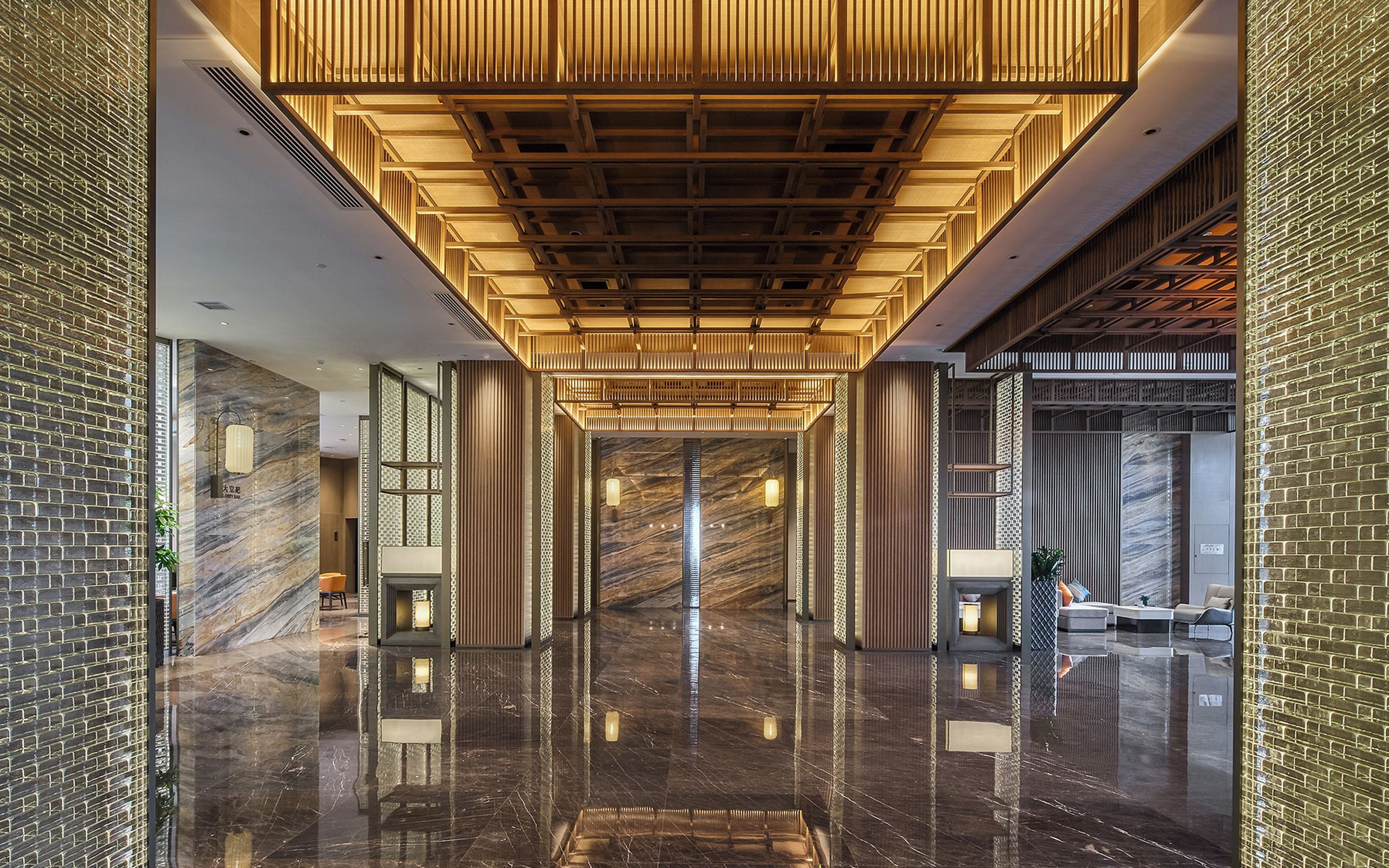 A modern hotel lobby with a reflective marble floor, wooden ceiling panels, and a brick wall.