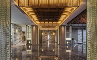 A modern hotel lobby with a reflective marble floor, wooden ceiling panels, and a brick wall.