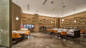 A modern restaurant interior with marble flooring, orange seating, and wooden shelving with decorative items.