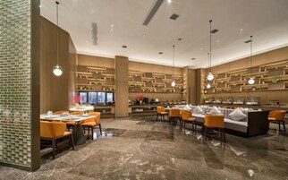 A modern restaurant interior with marble flooring, orange seating, and wooden shelving with decorative items.