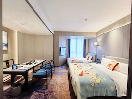 Habitación de hotel con cama, escritorio y silla. Hay un televisor en la pared y una ventana con cortinas.
