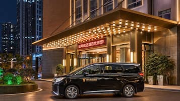 Una entrada de hotel moderna con una camioneta negra estacionada frente, señalización iluminada y una fachada bien iluminada.