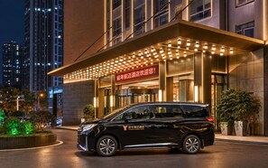 Una entrada de hotel moderna con una camioneta negra estacionada frente, señalización iluminada y una fachada bien iluminada.