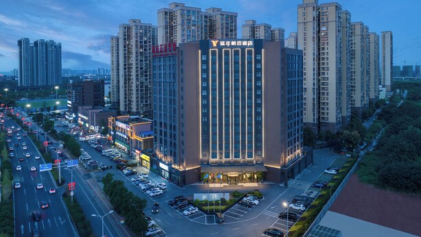 A multi-story hotel with a modern facade, surrounded by high-rise buildings and a busy street with parked cars. - Yannian Hangmai Hotel (Changsha)