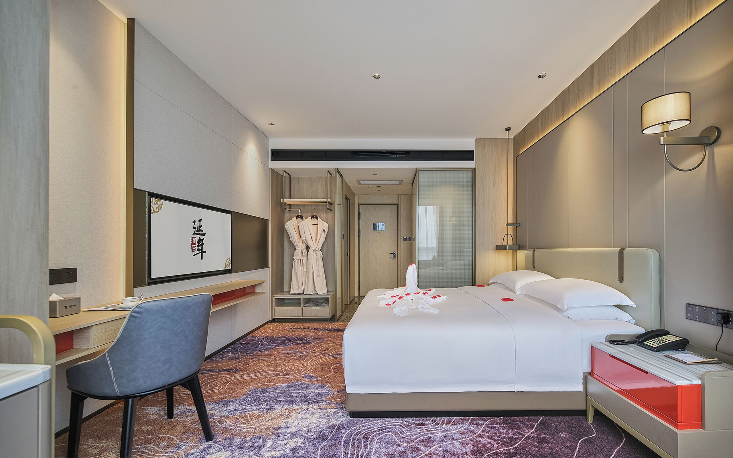Habitación de hotel con cama, mesita de noche, silla, escritorio y baño a la vista a través de una puerta abierta.