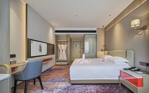 A hotel room with a bed, bedside table, chair, desk, and a bathroom visible through an open door.