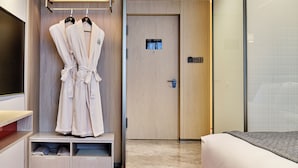 Een hotelkamer met een bed, een kledingrek met twee badjassen, een deur met een kaartsleuf en een klein plankje met spullen.