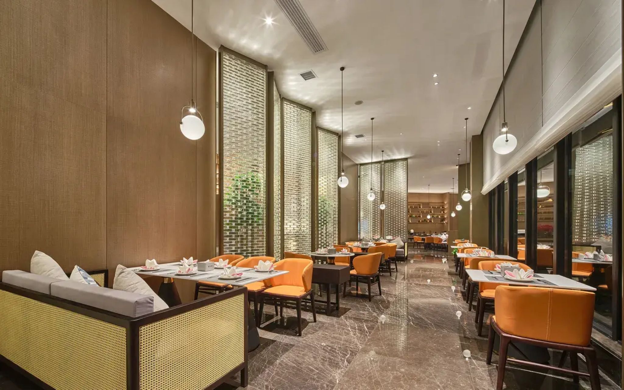 A restaurant with high tables and orange chairs, a marble floor, and a brick wall design.