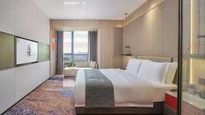 Een hotelkamer met een groot bed, uitzicht op de stad en een traditioneel Chinees kunstwerk aan de muur.