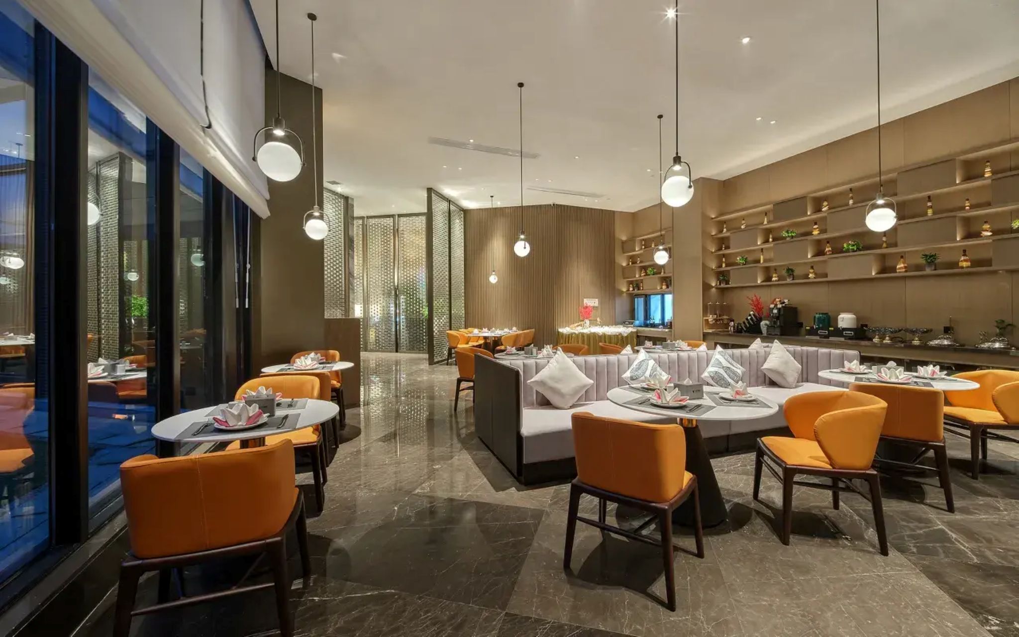Un interior de restaurante moderno con mesas redondas, sillas anaranjadas y una zona de bar.