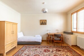 A bedroom with a bed, a desk, a chair, a wardrobe, a radiator, and a window with blinds. - Stylish Notting Hill Two Bed near Bayswater (London)