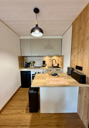 A compact kitchen with a central island, wooden cabinets, a built-in oven, and a coffee machine. - Chamrousse CAP 2000 Apartment (Chamrousse)